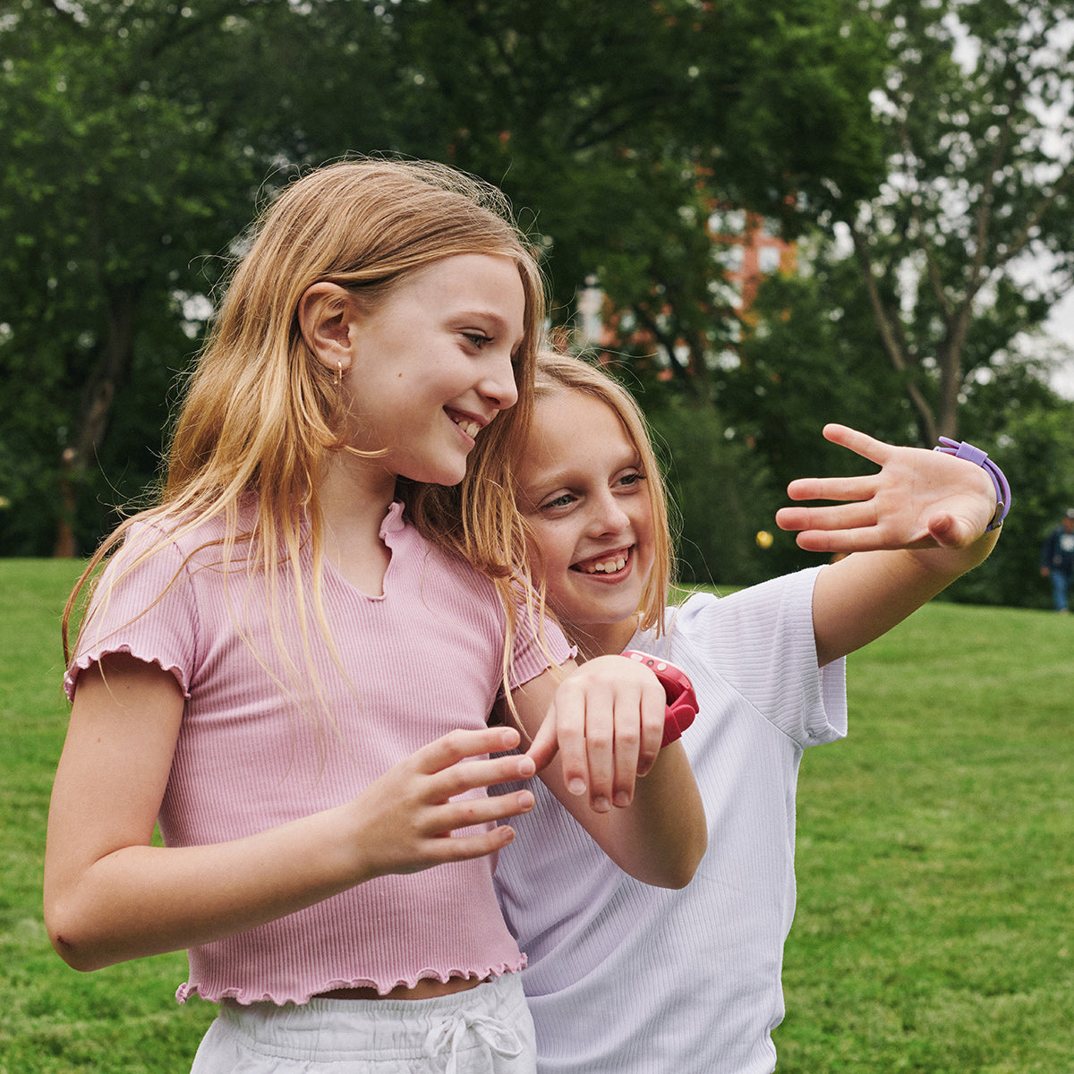 Two young girls standing outdoors in a park, smiling and interacting with each other.