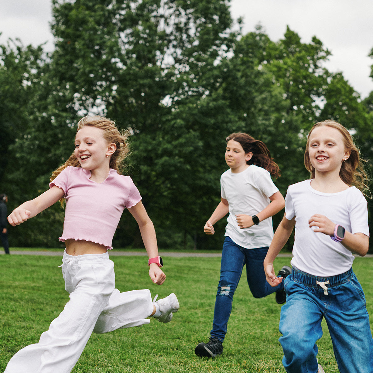 Three children running on a grassy field with trees in the background